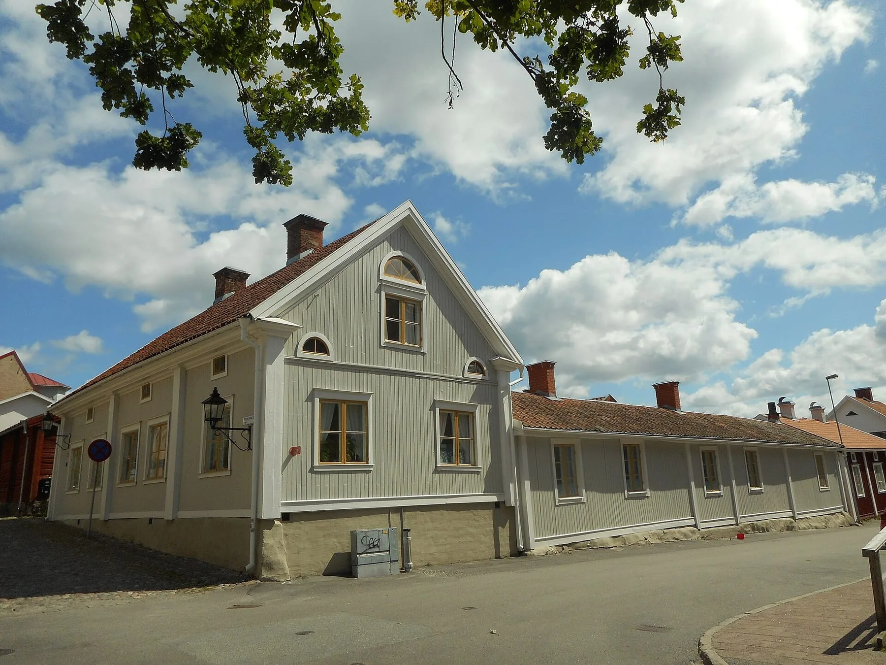 Ljusgrått trähus med vindskupor på Borgmästargatan i Nora, med en lång rad låga uthus längs gatan