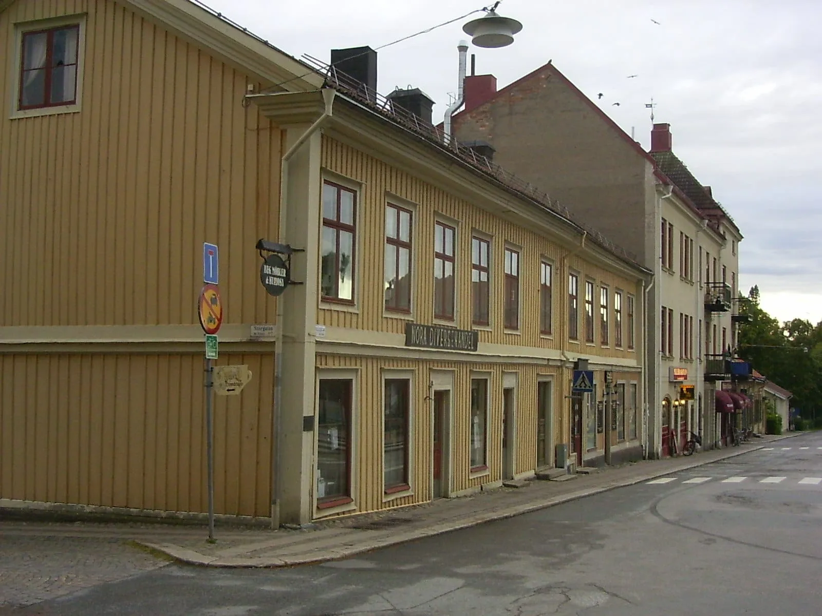 Gult panelklätt trähus i två våningar i ett gathörn i centrala Nora, med fler trähus längs gatan